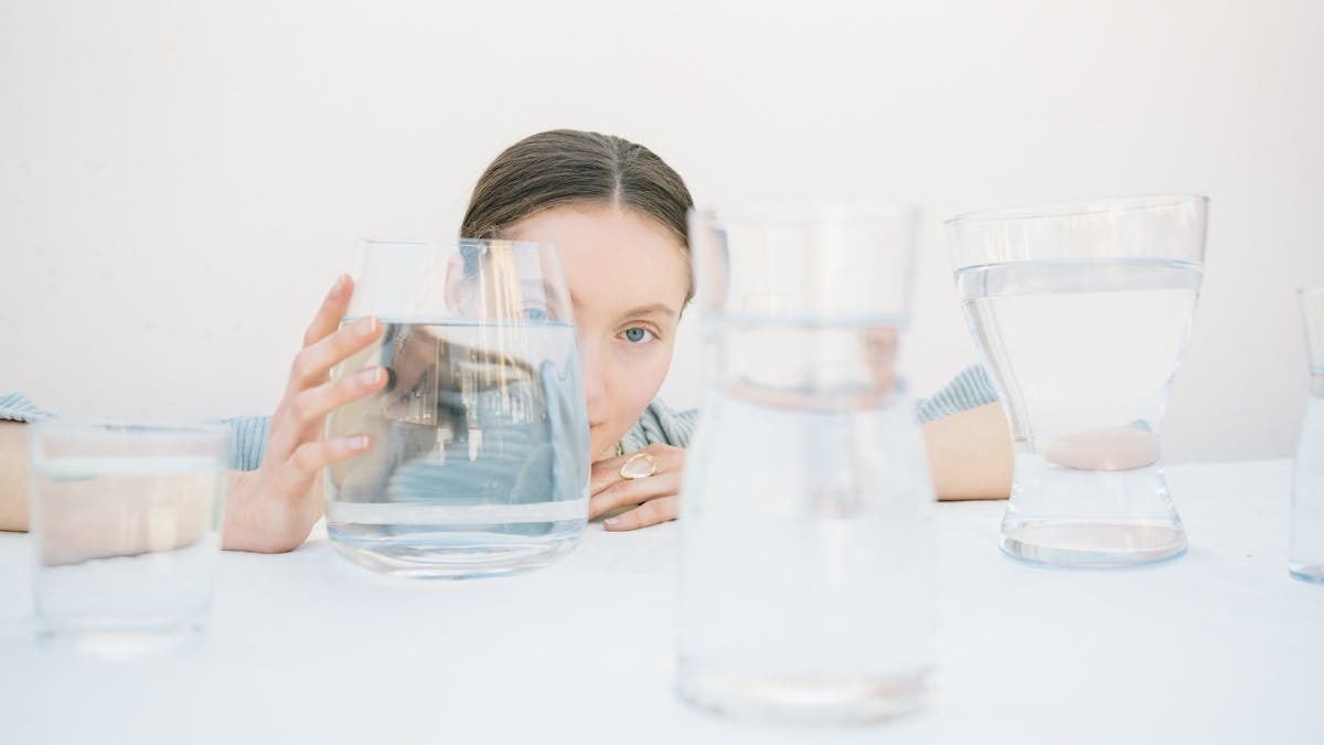 A woman peers through glasses filled with water, creating optical effects.